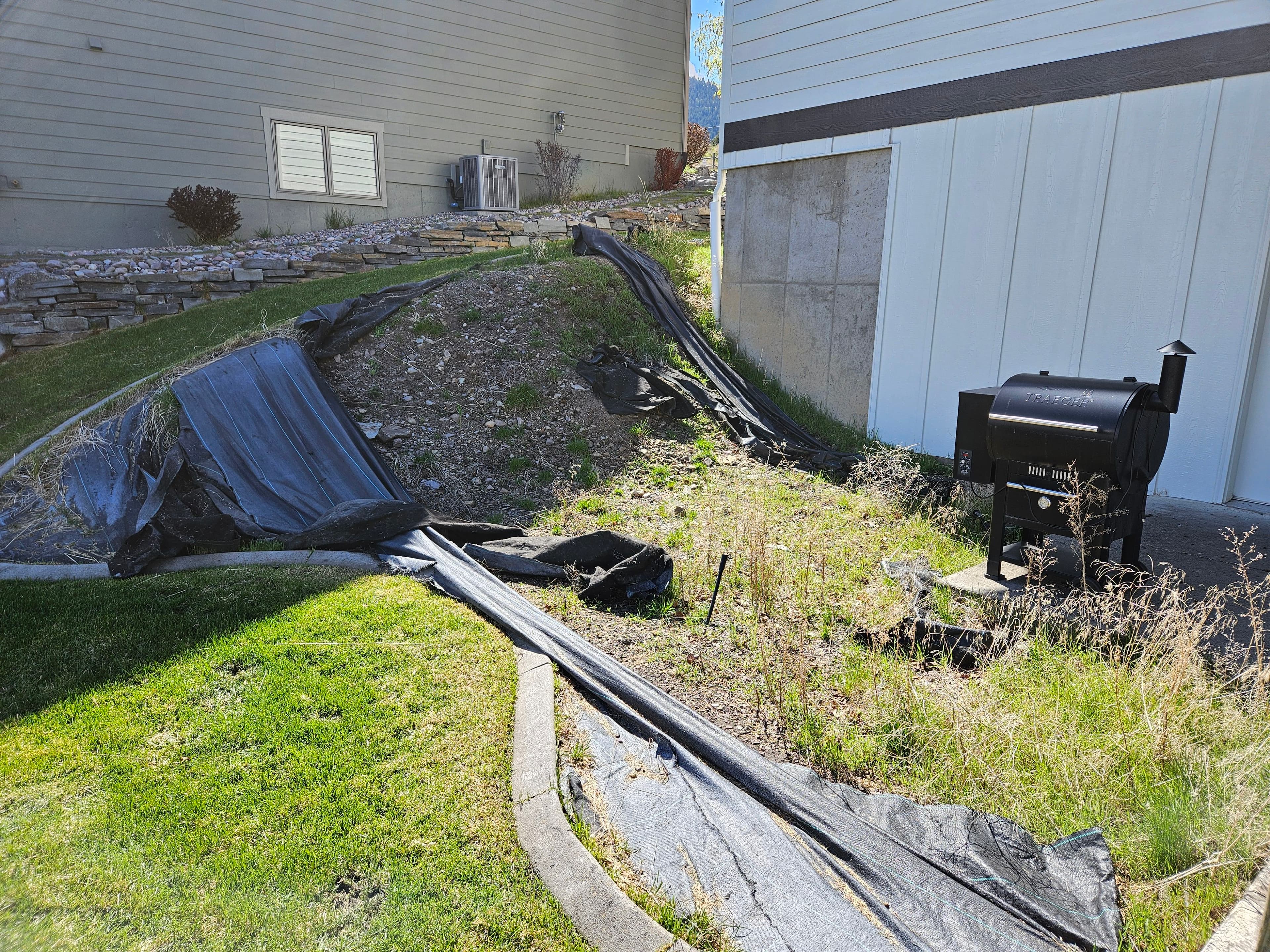 Damaged landscaping with black fabric and a grill in a residential yard.