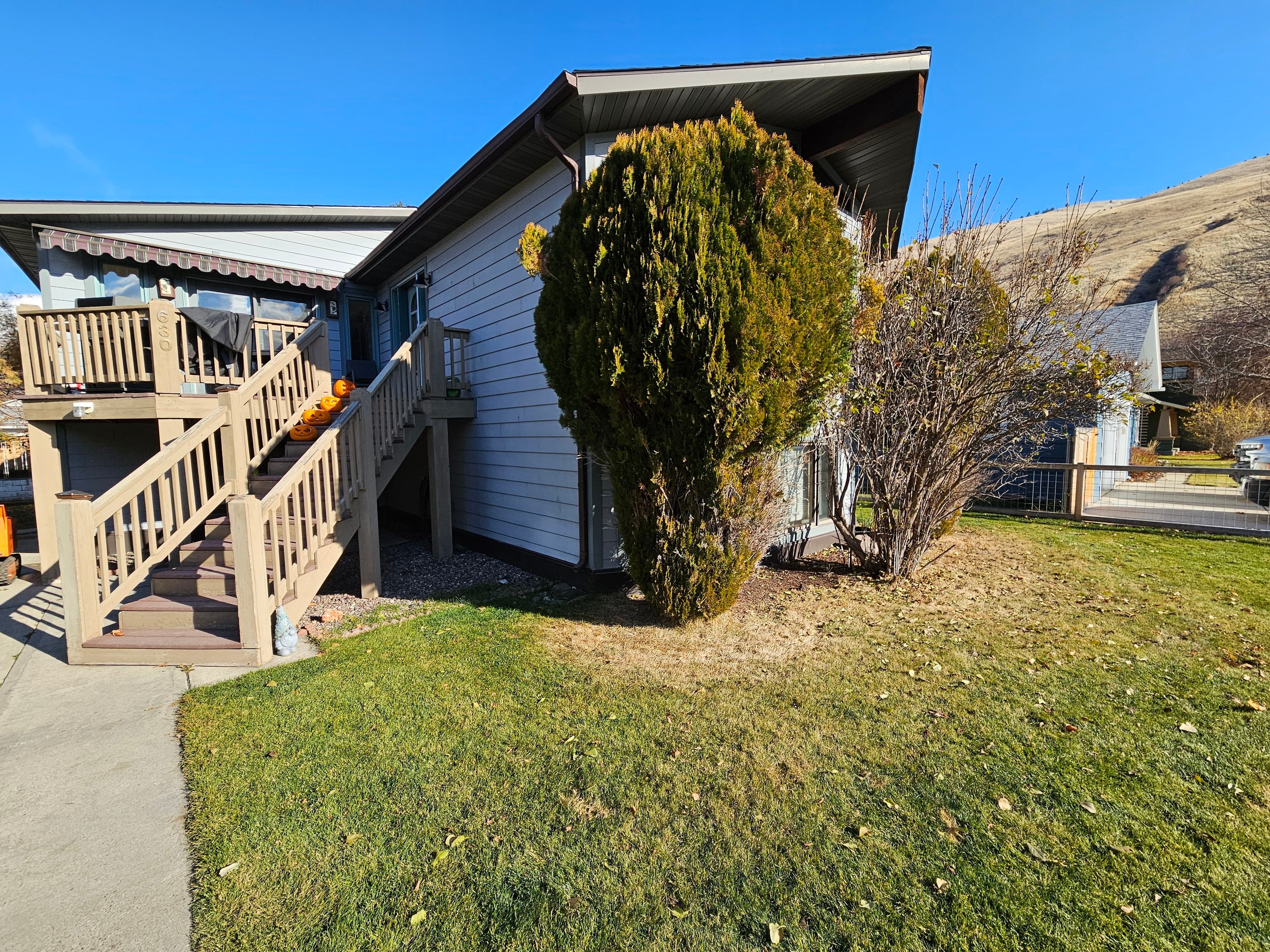 Two-story house with a sloped roof, green lawn, and decorative plants under clear blue sky.
