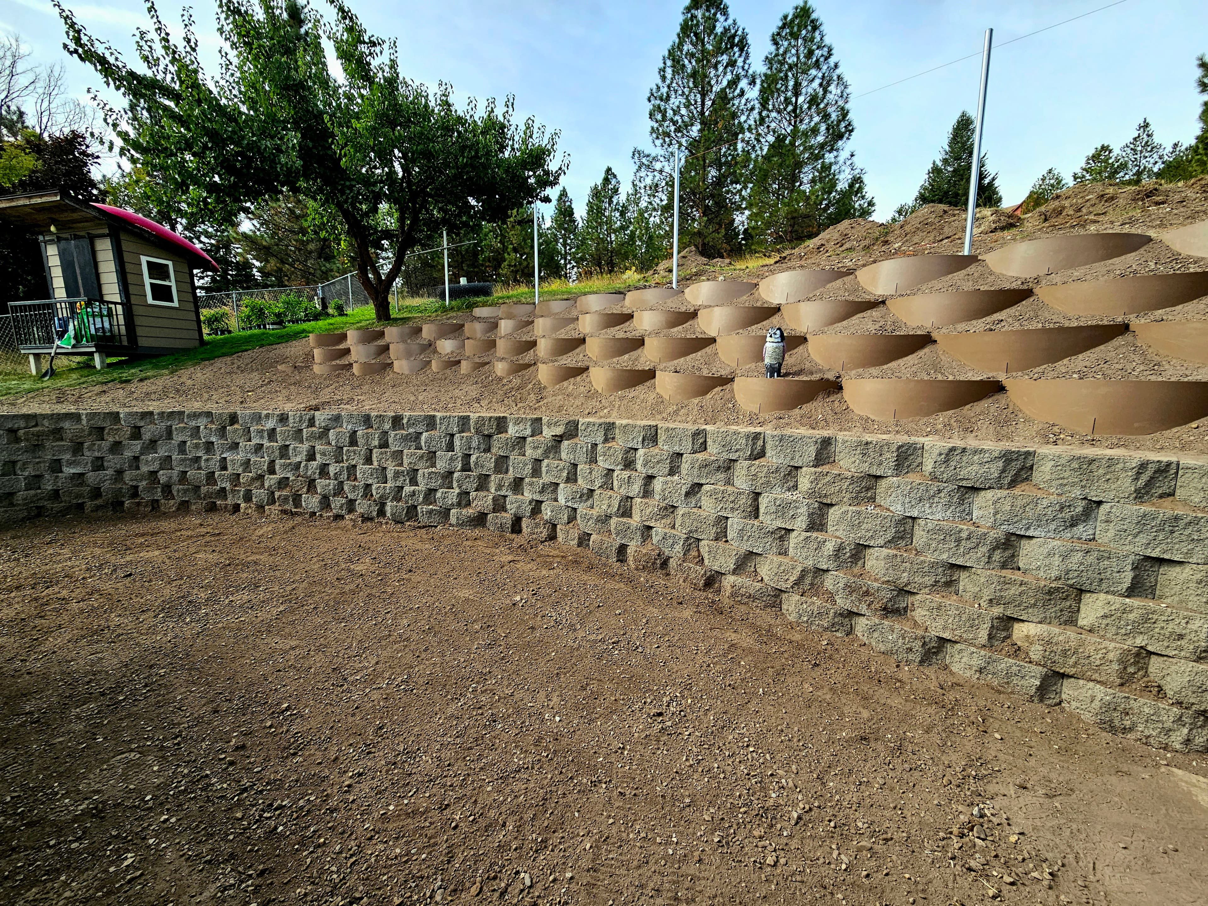 Garden with circular raised planters and a stone retaining wall, surrounded by trees and a shed.