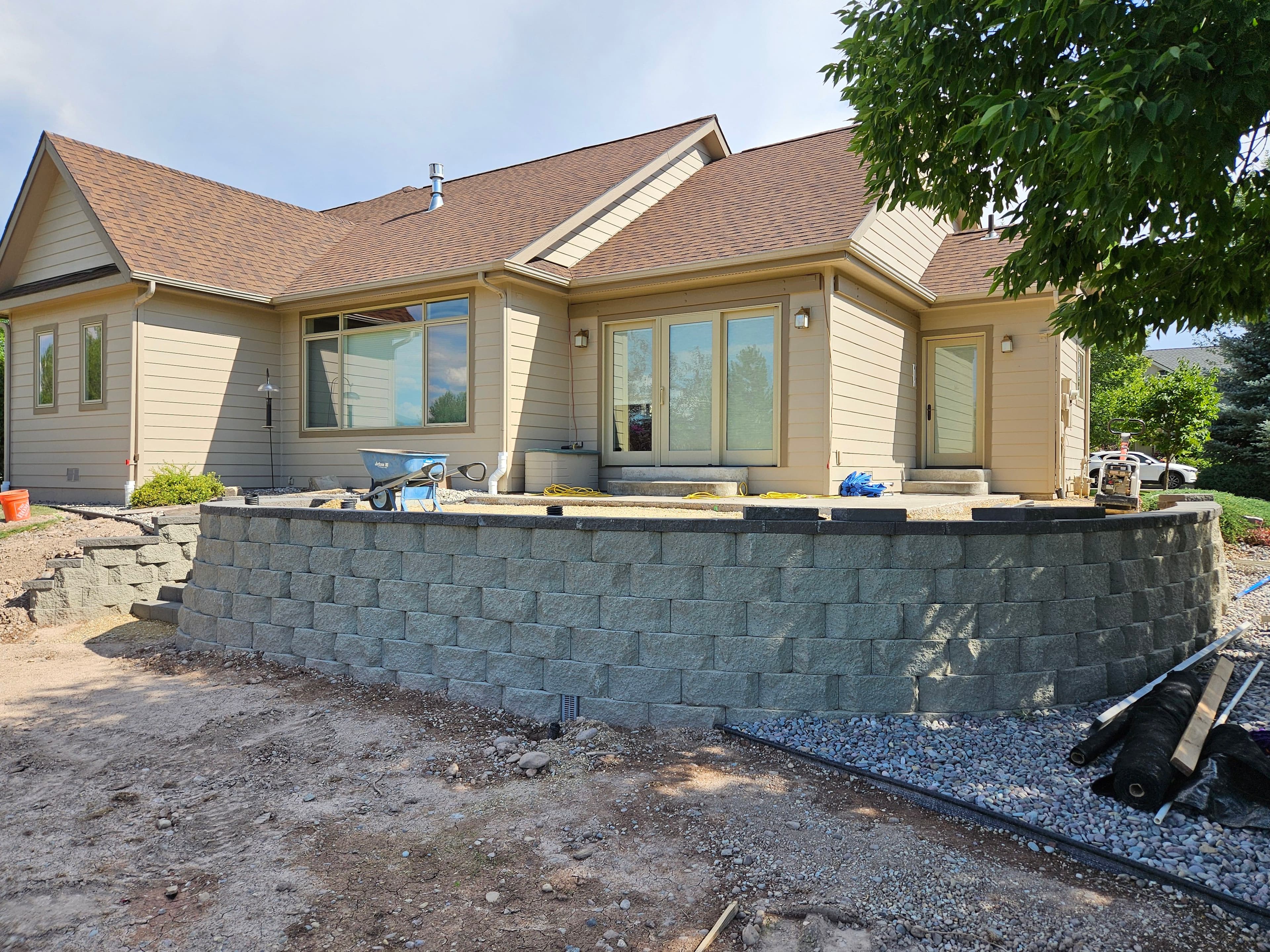 Home exterior with gray stone retaining wall, new landscaping, and construction tools visible.
