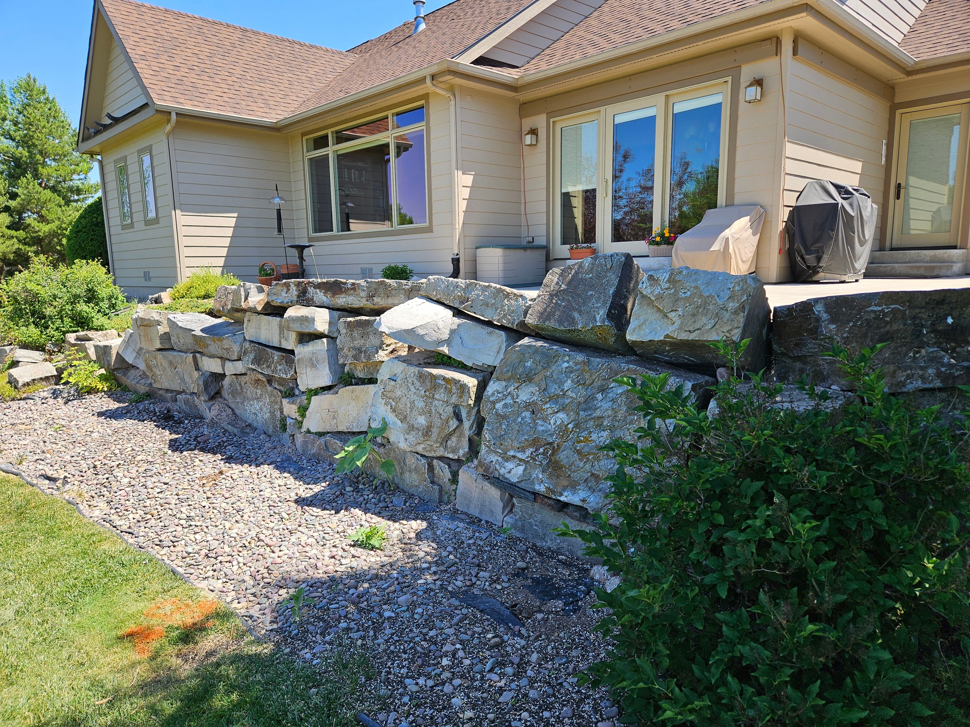 Rock retaining wall beside a house with a landscaped yard and patio area.