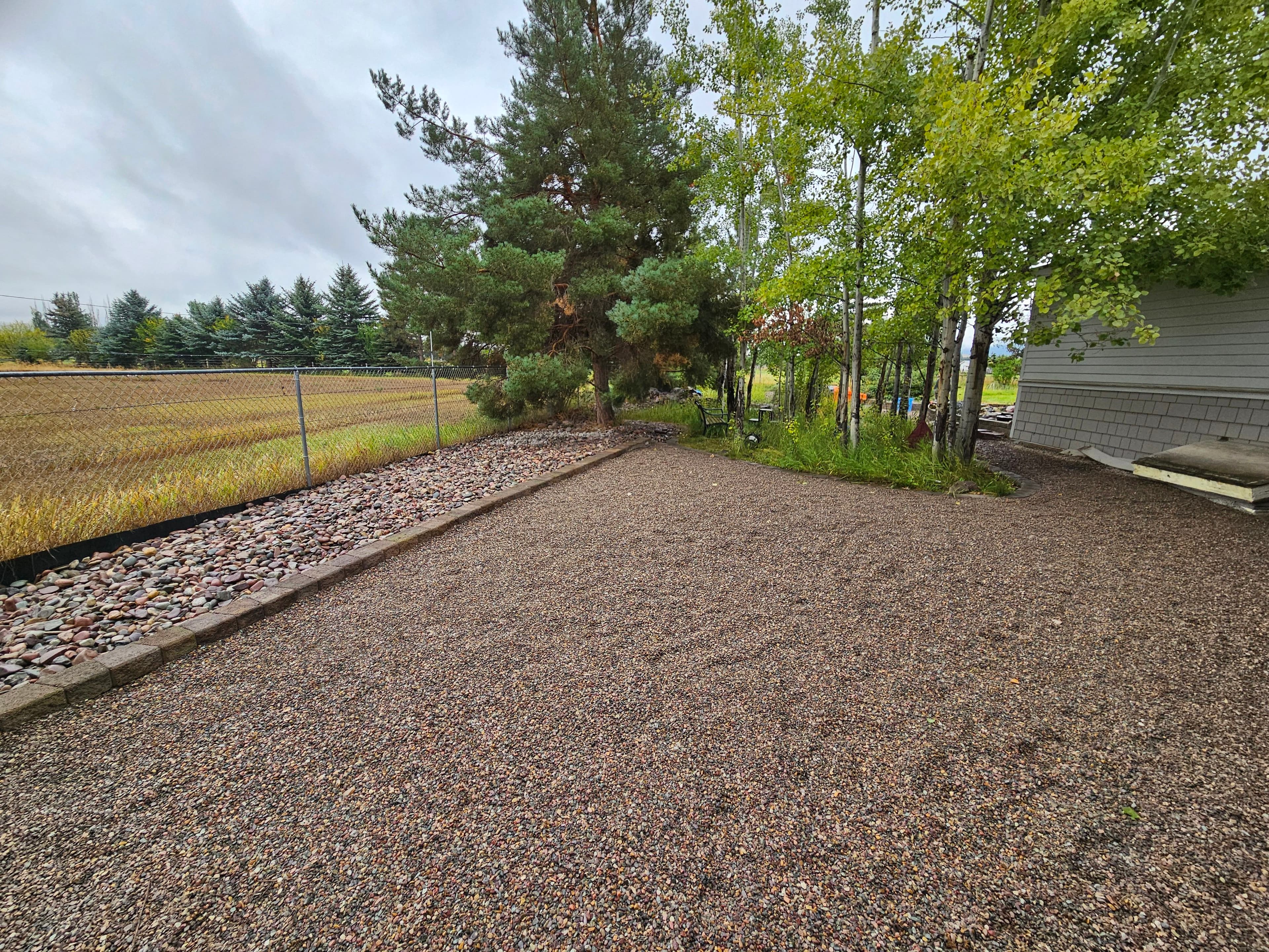 Gravel outdoor space beside trees and a field, creating a serene landscape.