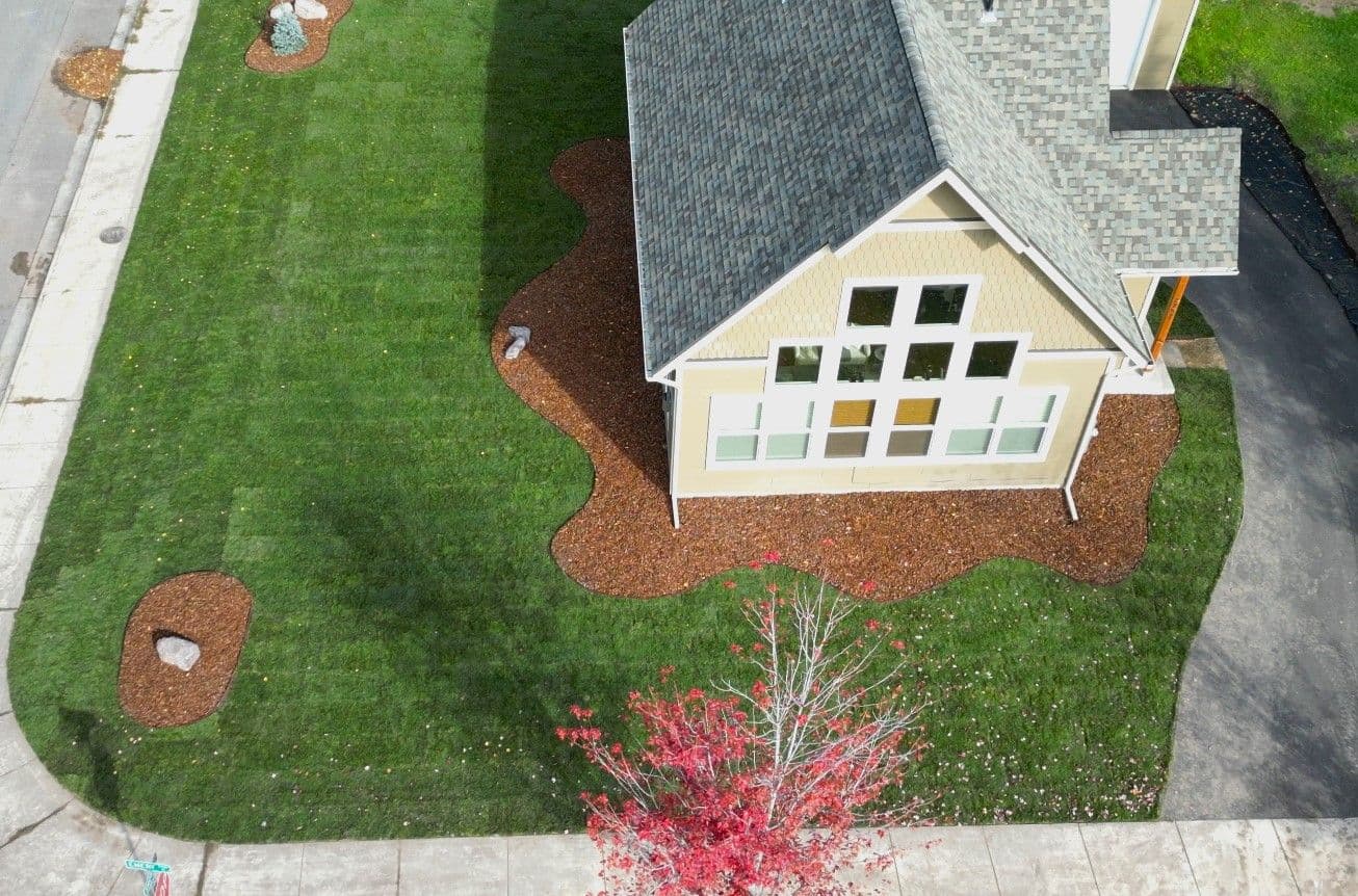 Aerial view of a modern house with landscaped yard featuring grass, mulch, and decorative stones.