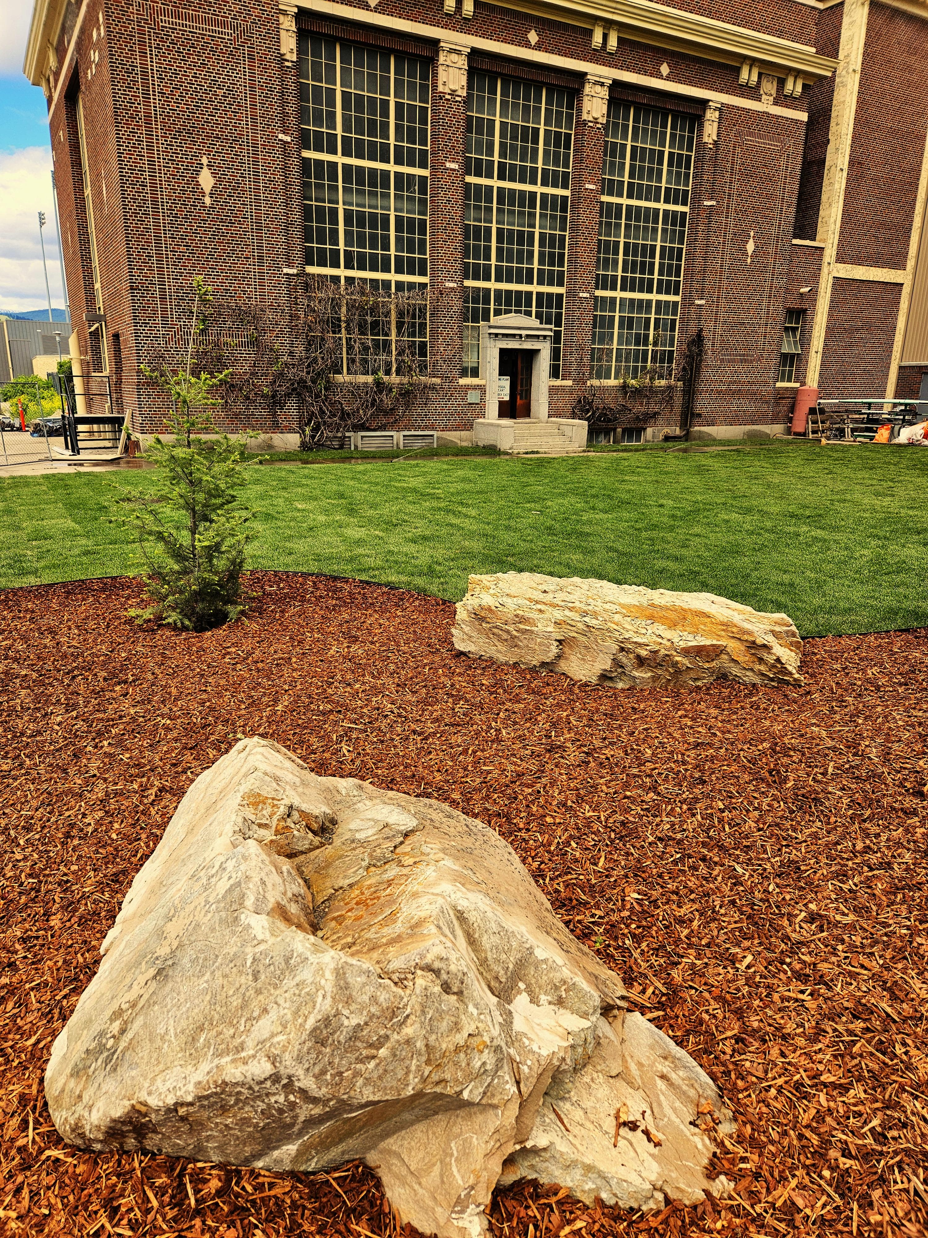 Large rocks in foreground with a historic brick building backdrop and green lawn.