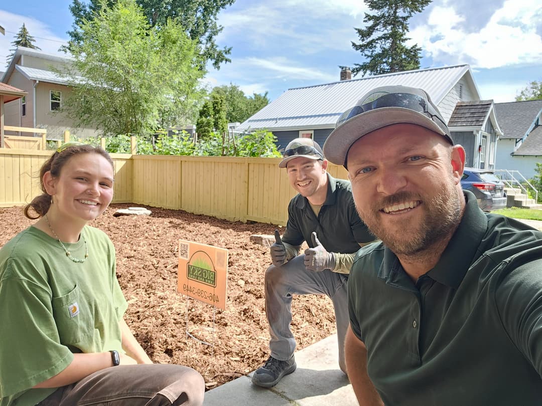 Landscaping team smiles beside new garden area; sign indicates project completion.