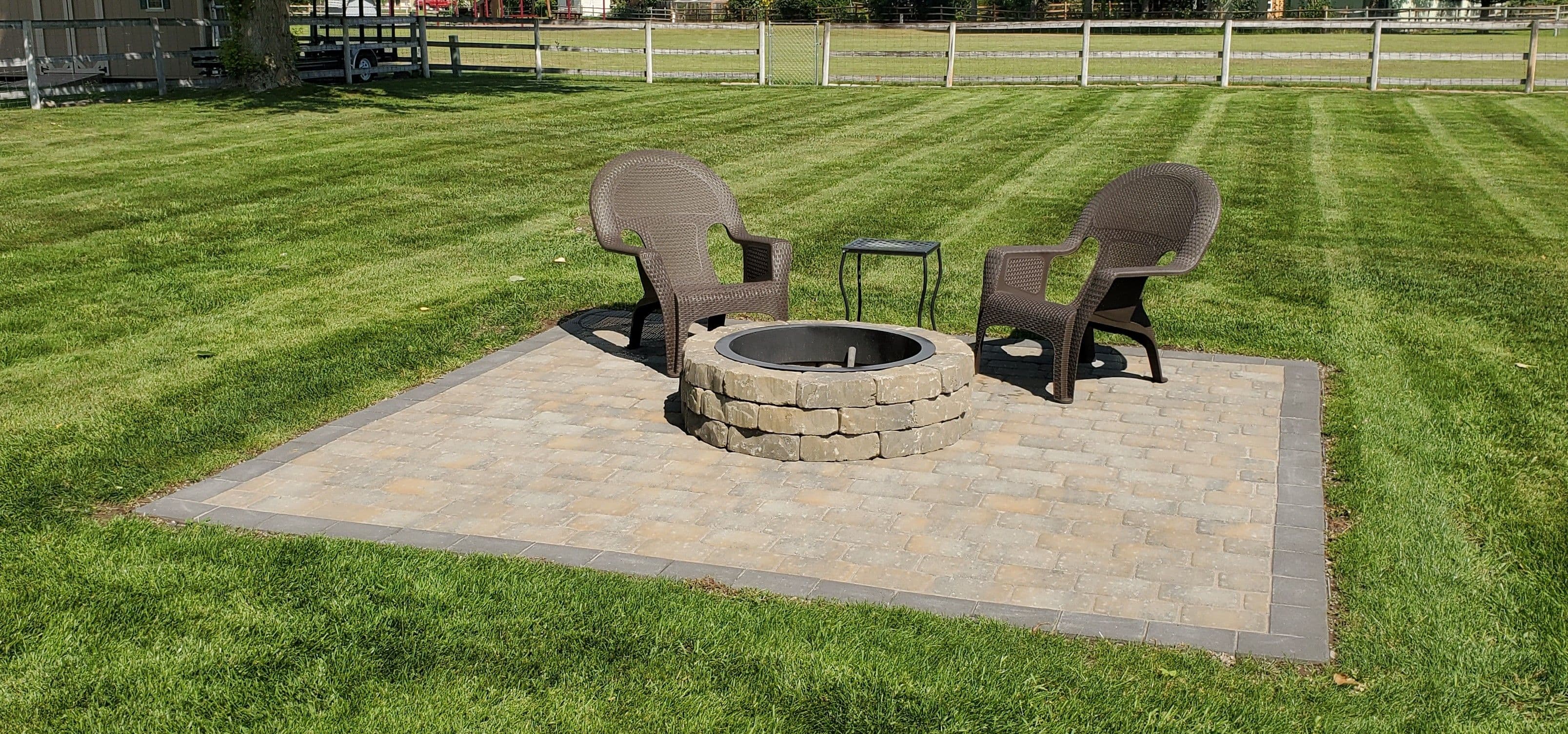 Outdoor seating area with two chairs and a fire pit on a landscaped lawn.