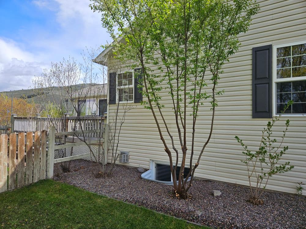 Side view of a home with landscaped yard, bushes, and a wooden fence.